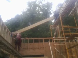 Carpenter raising a rafter beam on a new second story frame in Norwalk