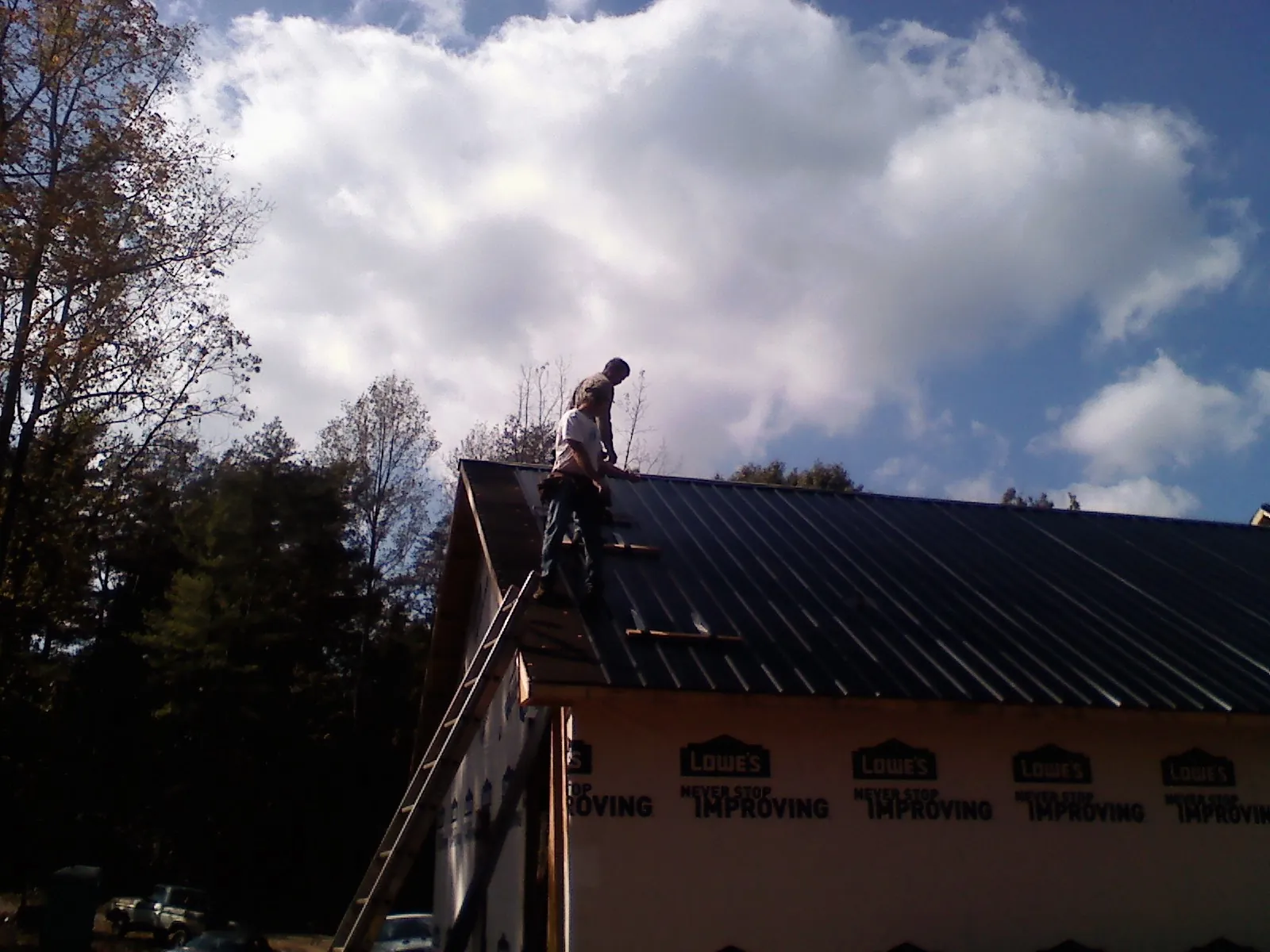 Roofer fastening dark metal panels high against a cloudy sky, from a Roof Inspection job in Norwalk