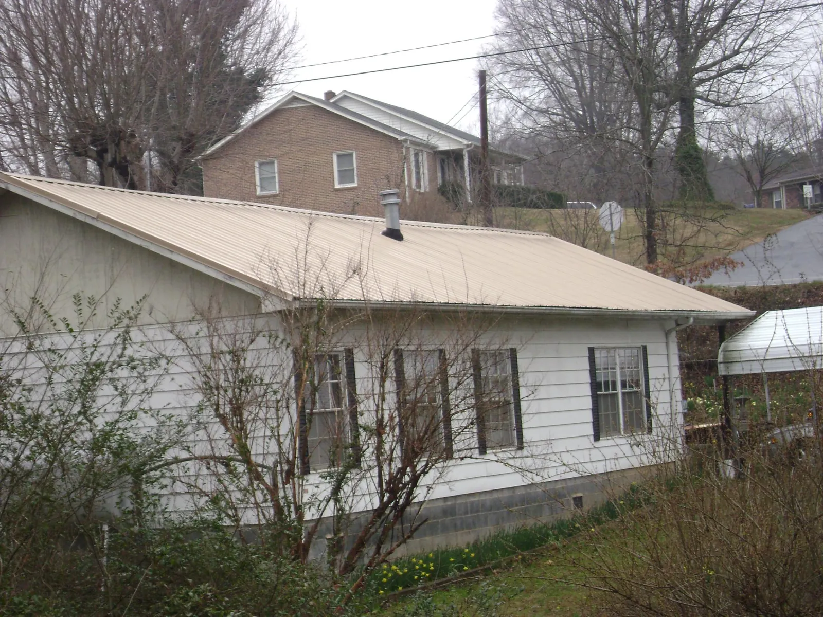 Tan metal roof on a white sided house set into a hillside — Commercial Roofing by Roofing Brothers in Norwalk